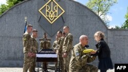 A serviceman offers the Ukrainian flag to the daughter of Yuriy Huk, a Ukrainian serviceman, killed during the Russian invasion of Ukraine, at his funeral service at the Saints Peter and Paul Garrison Church, in the western Ukrainian city of Lviv, May 16,