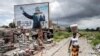 FILE - A woman walks past a torn billboard of former president of Guinea, Alpha Conde, in Conakry, Sept. 16, 2021.