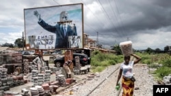 FILE - A woman walks past a torn billboard of former president of Guinea, Alpha Conde, in Conakry, Sept. 16, 2021.