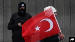 3일 터키 이스탄불에서 한 남성이 국기를 들고 새해에 발생한 테러 현장을 지키고 있는 경찰 앞을 지나고 있다.