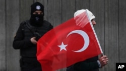 Một người đàn ông cầm cờ Thổ Nhĩ Kỳ đi ngang qua một viên cảnh sát đang bảo vệ hiện trường vụ tấn công ngày đầu năm ở Istanbul, Thổ Nhĩ Kỳ, 3/1/2017.