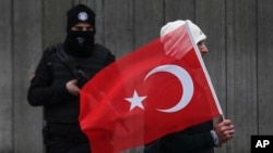 A man with a Turkish flag walks past a Turkish police officer guarding the scene, during a memorial outside the Reina club following the New Year's day attack, in Istanbul, Turkey, Jan. 3, 2017. 