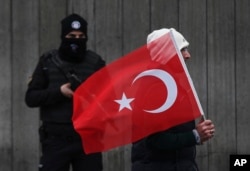 FILE - A man with a Turkish flag walks past a Turkish police officer guarding the scene, during a memorial outside the Reina club following the New Year's day attack, in Istanbul, Turkey, Jan. 3, 2017.