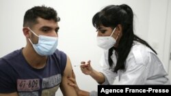 FILE - A young man receices a COVID-19 vaccine shot at a 24-hours vaccination center in Sarrola-Carcopino on the French Mediterranean island of Corsica, Jan. 8, 2022. 