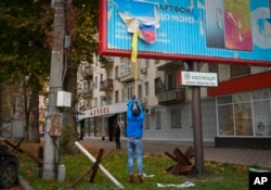 A local resident removes the Russian flag from a billboard in central Kherson, Ukraine, Sunday, Nov. 13, 2022.