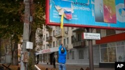 Lokalni stanovnik uklanja rusku zastavu s reklamnog panoa u  Hersonu, Ukrajina, nedjelja, 13. studenog 2022.