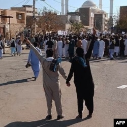 This image UGC image posted on Twitter on Nov. 11, 2022 shows two Iraninan men holding hands and showing the victory sign during protests in Zahedan, the capital city of Iran's Sistan-Baluchistan province. (Photo by UGC /AFP)