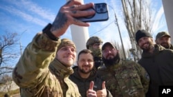 In this photo provided by the Ukrainian Presidential Press Office and posted on Facebook, Ukrainian soldiers take a selfie with President Volodymyr Zelenskyy, centre, during his visit to Kherson, Ukraine, Monday, Nov. 14, 2022. (Ukrainian Presidential Pre