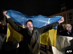 Seorang pria memegang bendera Ukraina saat orang-orang berkumpul di Lapangan Maidan untuk merayakan pembebasan Kherson, di Kyiv pada 11 November 2022. (Foto: AFP)