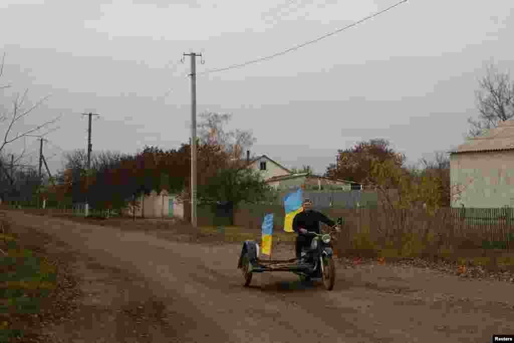 Guru Yurii Nevolchuk mengendarai sepeda motornya dengan bendera nasional Ukraina di desa Blahodatne di wilayah Kherson, yang direbut kembali dari Rusia oleh pasukan Ukraina sehari sebelumnya.