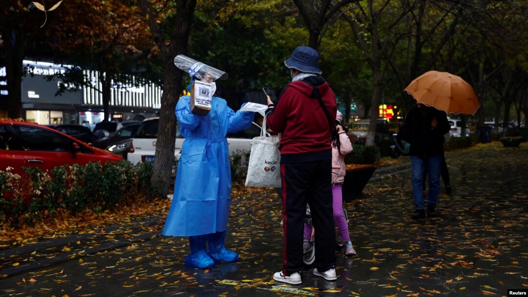 A worker in a protective suit guides people to scan health QR code at a nucleic acid test booth for the coronavirus disease (COVID-19), in Beijing, China, Nov. 11, 2022. 
