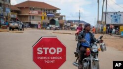 FILE - A man drives a motorcycle past a police checkpoint set up to stop motorcycles carrying passengers, in an attempt to limit the spread of Ebola, in Mubende, Uganda Nov. 1, 2022.