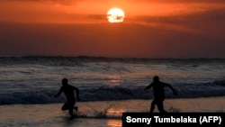Dua orang tampak berkejar-kejaran di laut saat matahari terbenam di Pantai Mesari, Seminyak, Bali pada 21 Juni 2022. (Foto: AFP/Sonny Tumbelaka)