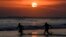 Dua orang tampak berkejar-kejaran di laut saat matahari terbenam di Pantai Mesari, Seminyak, Bali pada 21 Juni 2022. (Foto: AFP/Sonny Tumbelaka)