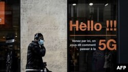 FILE - A man talks on a mobile phone as he walks past a store of French telecom group Orange advertising the 5G service on its shop window, in Bordeaux, southwestern France, on February 23, 2021.