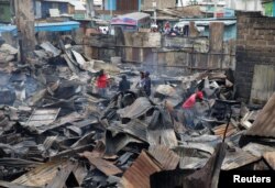 People inspect the damage as they stand amid the remains of properties that were burned by rioters in Kawangware slums in Nairobi, Kenya, Oct. 28, 2017.