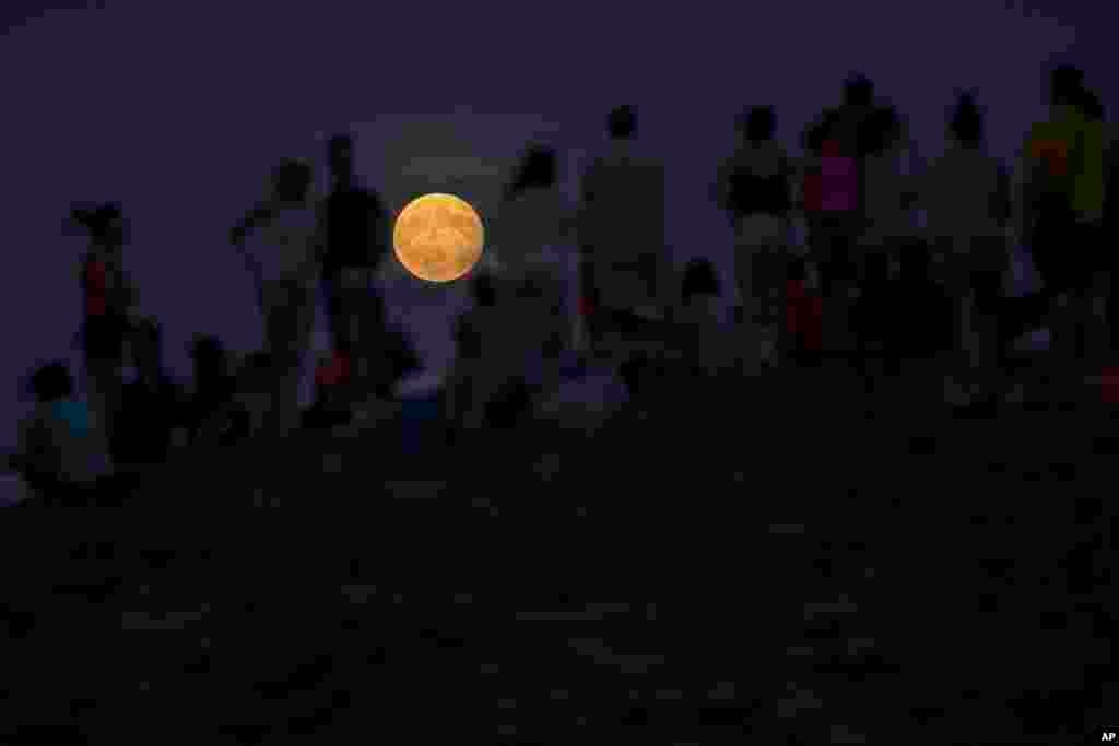 People watch a rising full moon during a partial lunar eclipse, from atop a hill at the Tio Pio park in Madrid, Spain, Aug. 7, 2017.