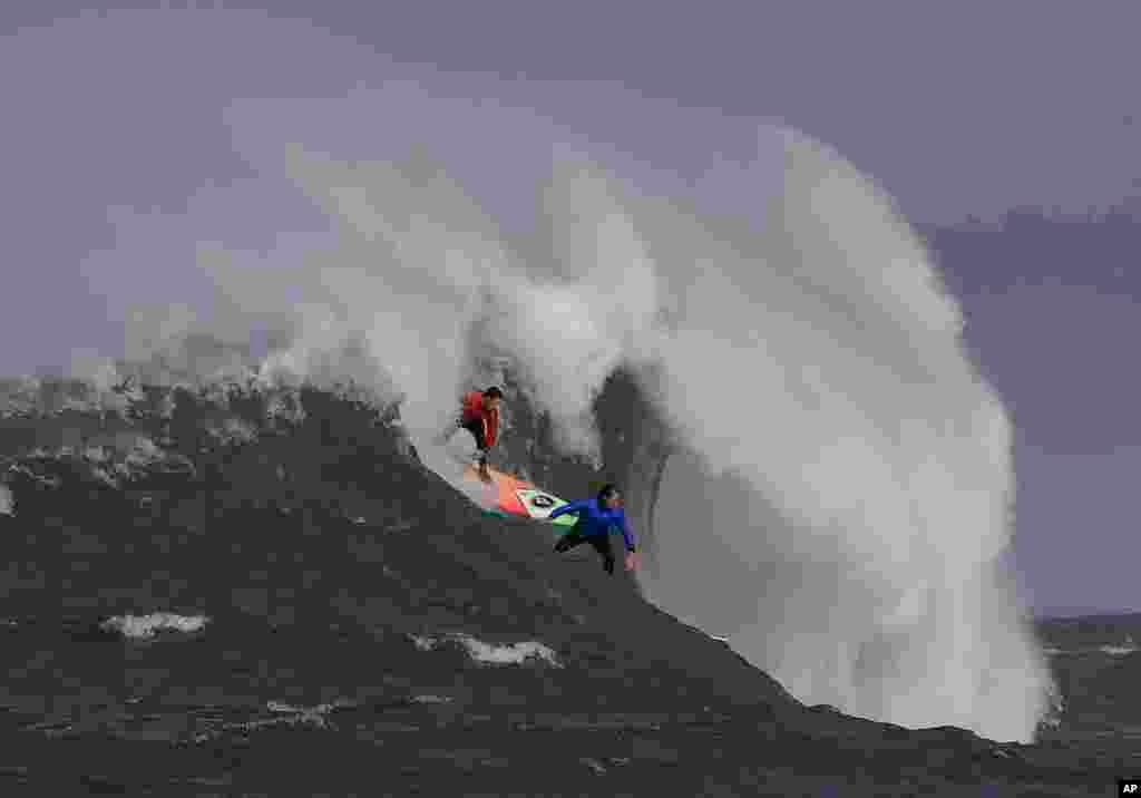 Ken Collins, left, and Chris Bertish surf a giant wave during the second heat of the Mavericks surfing contest in Half Moon Bay, California.