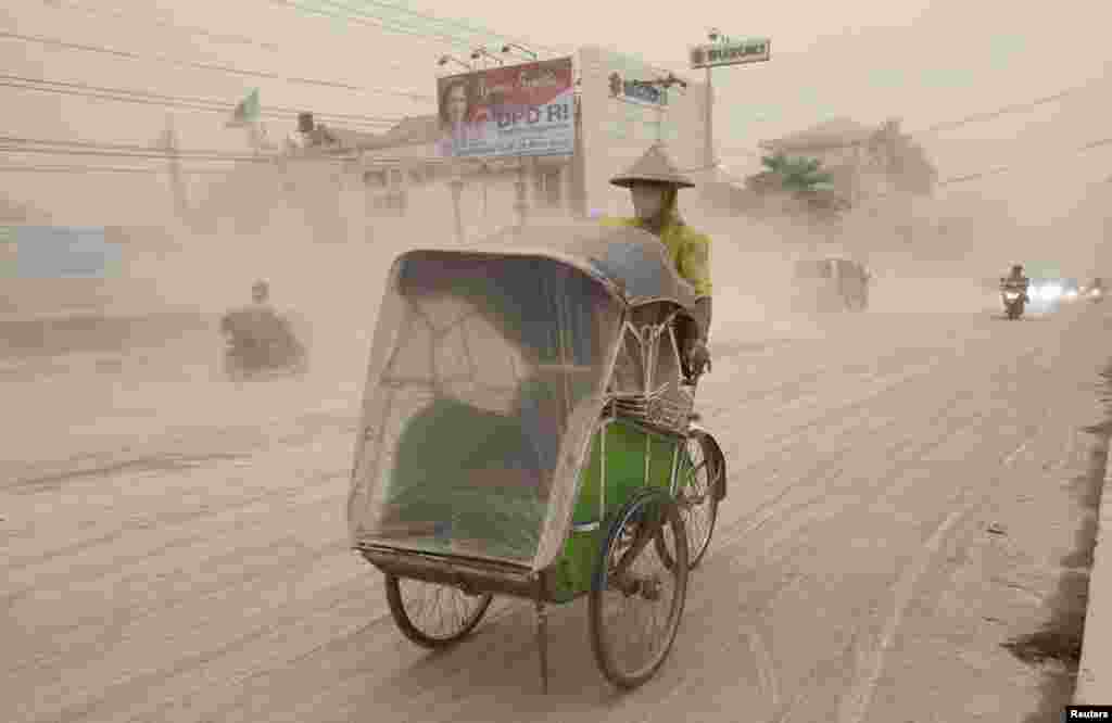 A man wears a mask as he rides a becak, a kind of rickshaw, on a road covered with from Mount Kelud, in Yogyakarta, Feb. 14, 2014.