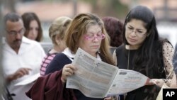 Voters read the a sample ballot as they wait in line to cast their vote in Hialeah, Florida, November 6, 2012.