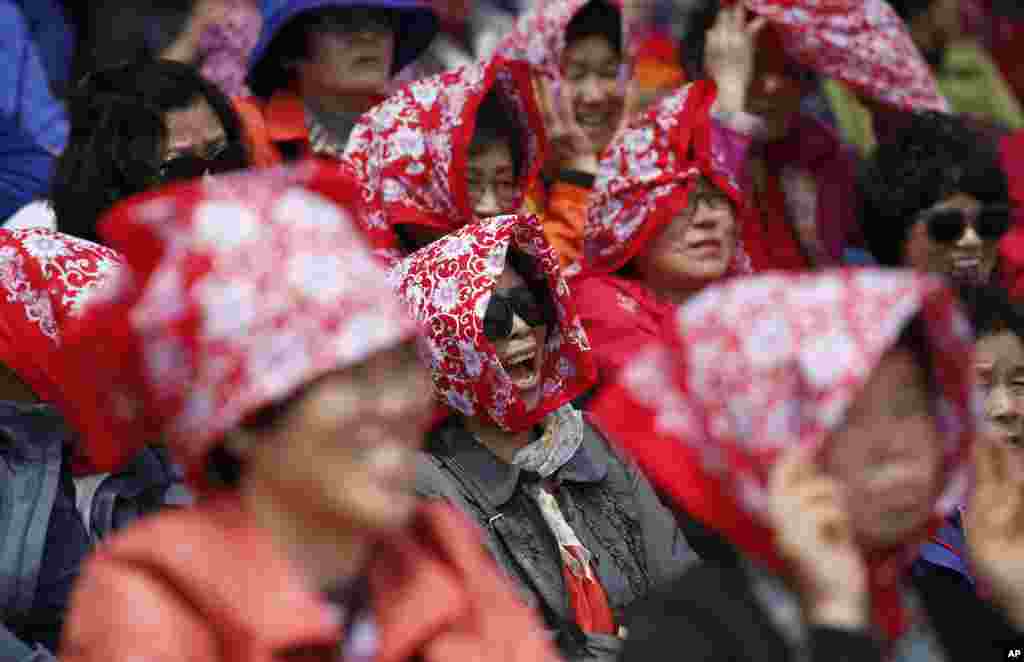 South Korean women smile as they cover their heads with scarves against the sun and wind before a weekly demonstration of the military honor guard at the War Memorial of Korea in Seoul. The demonstrations resumed after being suspended during the winter.