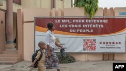 Mãe e filho passam ao lado de um cartaz de campanha do Movimento Popular de Libertação, Cotonu, Benin, 6 Janeiro 2023 