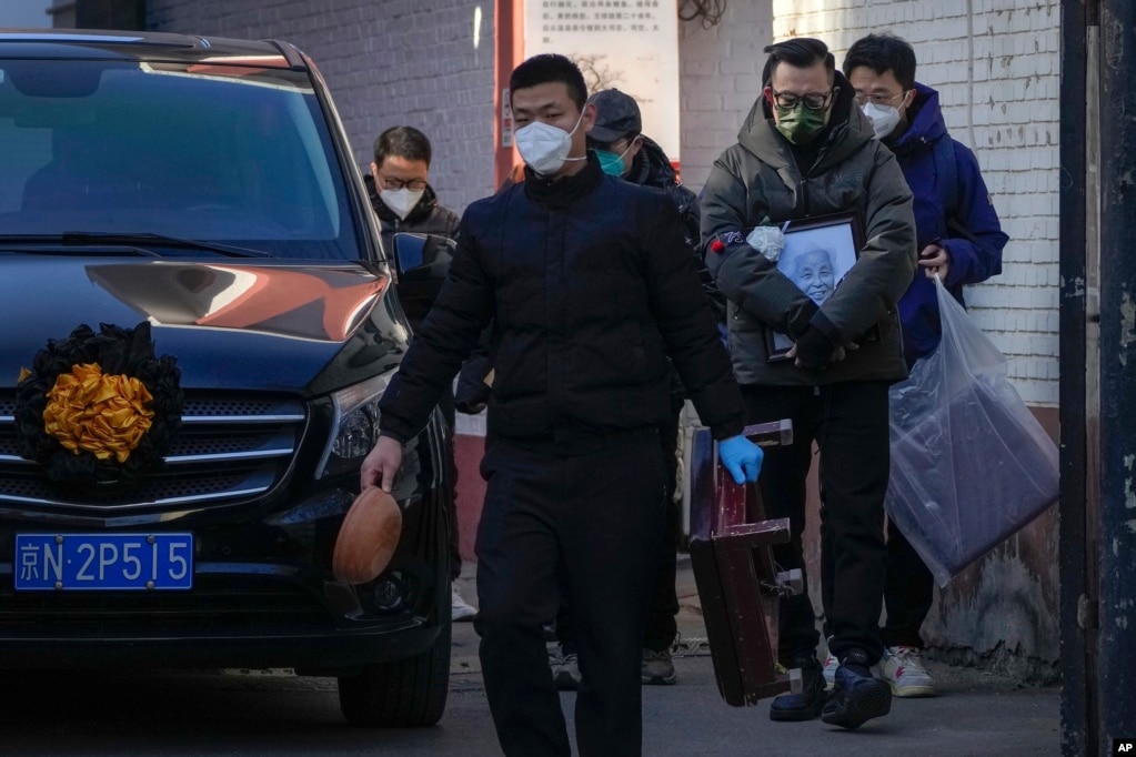 北京一个发热门诊外，一名亲属手拿去世亲人的照片走过一辆灵车。（2022年12月19日）(photo:VOA)