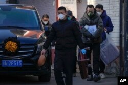 北京一個發熱門診外，一名親屬手拿去世親人的照片走過一輛靈車。（2022年12月19日）