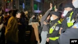 This frame grab from eyewitness video footage made available via AFPTV on November 27, 2022 shows demonstrators shouting slogans as police hold their positions, in Shanghai.