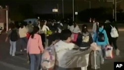 FILE - In this photo taken from video footage and released by Hangpai Xingyang, people with suitcases and bags are seen leaving from a Foxconn compound in Zhengzhou in central China's Henan Province on Oct. 29, 2022.