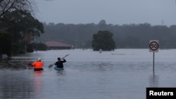 FILE - James Taylor and Joshua Myers paddle kayaks down a flooded residential street on their way to check on a friend's home, after heavy rains inundated the area with floodwaters in the McGraths Hill suburb of Sydney, Australia, July 6, 2022. 