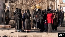 Afghan female university students, stopped by Taliban security personnel, stand next to a university in Kabul, Dec. 21, 2022.