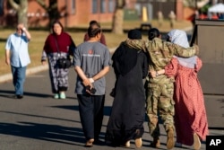 FILE - A female member of the military puts her arms around two female Afghan refugees at an Afghan refugee camp on Joint Base McGuire Dix Lakehurst, New Jersey, Sept. 27, 2021.