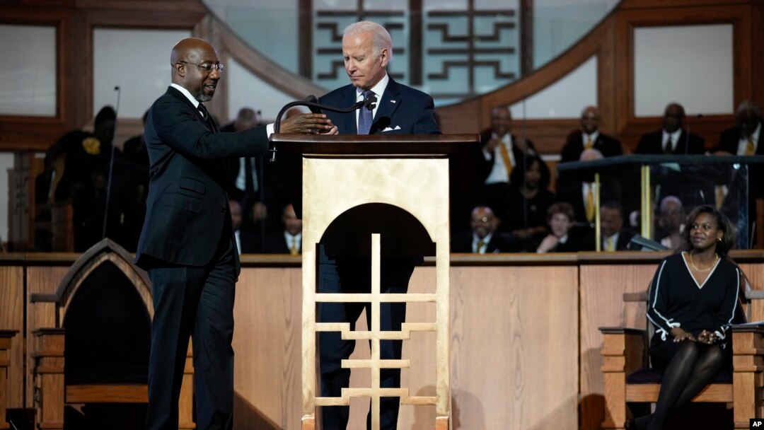 El senador Raphael Warnock, demócrata por Georgia., pastor principal de la Iglesia Bautista Ebenezer, ayuda al presidente Joe Biden con el micrófono en la Iglesia Bautista Ebenezer en Atlanta, el 15 de enero de 2023, durante un servicio en honor a Martin Luther King Jr.
