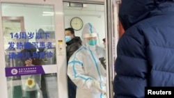 2022年12月15日，一名男子在北京一家醫院的發熱門診門外排隊等待。一位身著防護服的醫務人員正準備關門。中國有關當局毫無預兆地宣布解封後，新冠肺炎的感染人數和死亡人數不斷增加，引起人們的恐慌。