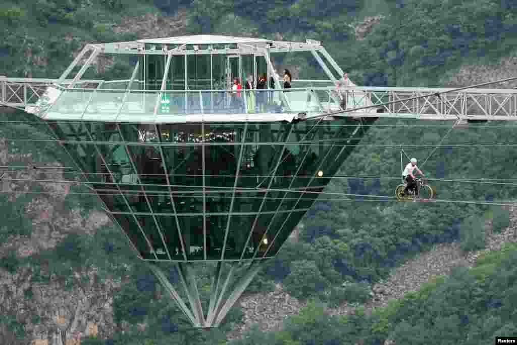 A man rides a bike on a zip line during the opening ceremony of the glass bridge over Dashbashi Canyon outside the town of Tsalka, Georgia, June 14, 2022.