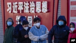 Residents wearing face masks wait in line for their routine COVID-19 tests along a wall displaying the words "Xi Jinping rule of law ideology learning ground" in Beijing, Monday, Dec. 5, 2022. (AP Photo/Andy Wong)