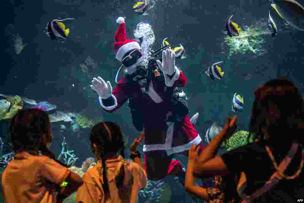 A diver dressed in a Santa Claus costume waves to young visitors at the Sea Life Bangkok Ocean World aquarium in Bangkok.