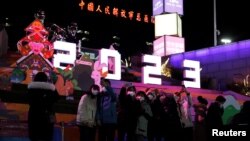 新年前夜，人们站在北京一座大型商场外“2023”字样的灯饰下，而此时新冠病毒正如潮水般在北京卷土重来。霓虹灯庆祝2023年广告背后远处是“中国人民解放军总医院”大楼。