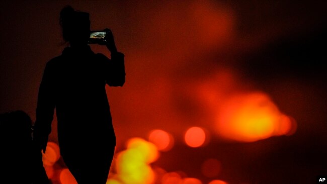 A woman records with her phone as lava erupts from the Mauna Loa volcano near Hilo, Hawaii, Dec. 1, 2022.