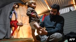 Mohammed, the father of Syrian Maya Merhi, sits next to his disabled toddler, inside the family tent at an Internally Displaced Persons (IDP) camp in Syria&#39;s rebel-held northwestern Idlib province, near the Bab al-Hawa border crossing with Turkey.