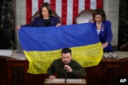 La vicepresidenta Kamala Harris y la presidenta de la Cámara de Representantes Nancy Pelosi, sostienen la bandera ucraniana firmada por soldados en el frente de batalla en Bakhmut, en la disputada provincia ucraniana de Donetsk, que el presidente de Ucrania Volodymyr Zelenskyy obsequió a los legisladores, durante un discurso de Zelenskyy en el Capitolio, el miércoles 21 de diciembre de 2022, en Washington.