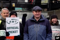 Mick Lynch, Sekjen Serikat Pekerja Kereta Api, Maritim dan Transportasi (RMT), (depan), bergabung dengan para pekerja kereta api dalam aksi mogok di luar stasiun Euston di London, Selasa, 13 Desember 2022. (AP/Kin Cheung)