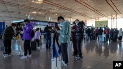 Masked travelers use their smartphones to fill in their health declaration after checking in at the international flight check in counter at the Beijing Capital International Airport in Beijing, Thursday, Dec. 29, 2022.