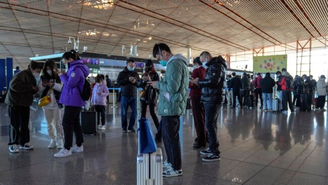 Masked travelers use their smartphones to fill in their health declaration after checking in at the international flight counter at the Beijing Capital International Airport in Beijing, Dec. 29, 2022.