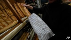 Bakery owner Florence Poirier puts baguettes in to a bag that reads, ' the real taste of bread,' for a customer at a bakery, in Versailles, west of Paris, Nov. 29, 2022.