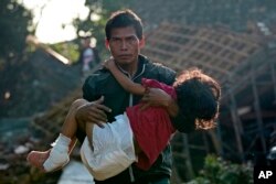 Seorang pria membawa putrinya yang terluka saat mereka menuju ke tempat penampungan sementara bagi mereka yang terlantar akibat gempa Senin di Cianjur, Jawa Barat, Kamis, 24 November 2022. (AP Photo/Tatan Syuflana)