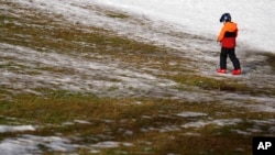 FILE - A child crosses a meadow with snow at a slope in Filzmoos, south of Salzburg, Austria, Jan. 5, 2023.