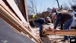 Belinda Penner, center, watches as Jr. Ibarra, left, and Jared Reaves, right, carry a beam from her cousin's tornado destroyed home, Dec. 13, 2022, in Wayne, Okla.