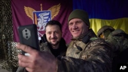 FILE - In this photo provided by the Ukrainian Presidential Press Office, a Ukrainian soldier takes a selfie with President Volodymyr Zelenskyy, left, in Sloviansk, Donbas region, Ukraine, Dec. 6, 2022. In a recent speech, Zelenskyy praised front-line workers.